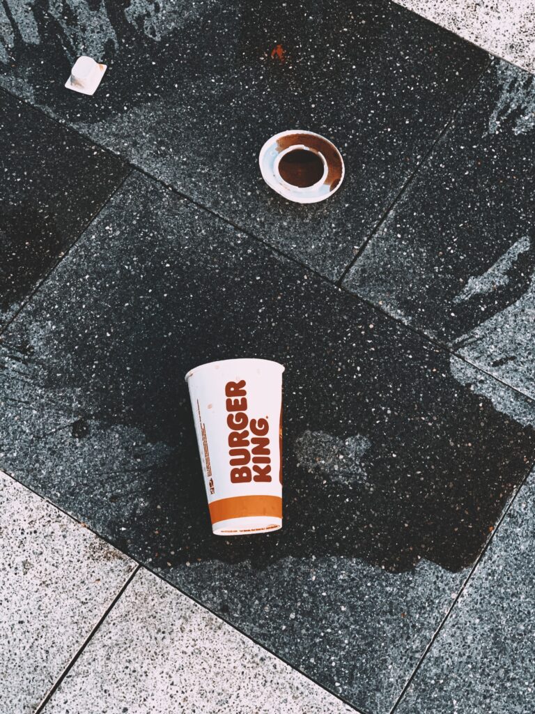 A Burger King paper cup lies overturned with a spill on a dark tiled floor. Urban littering concept.