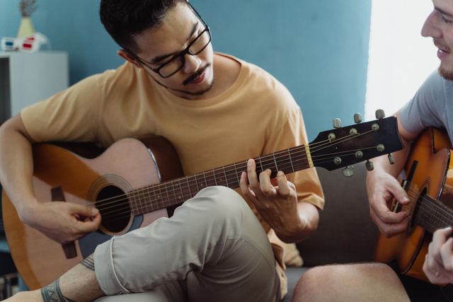 Two men enjoying a music session together, playing acoustic guitars indoors.